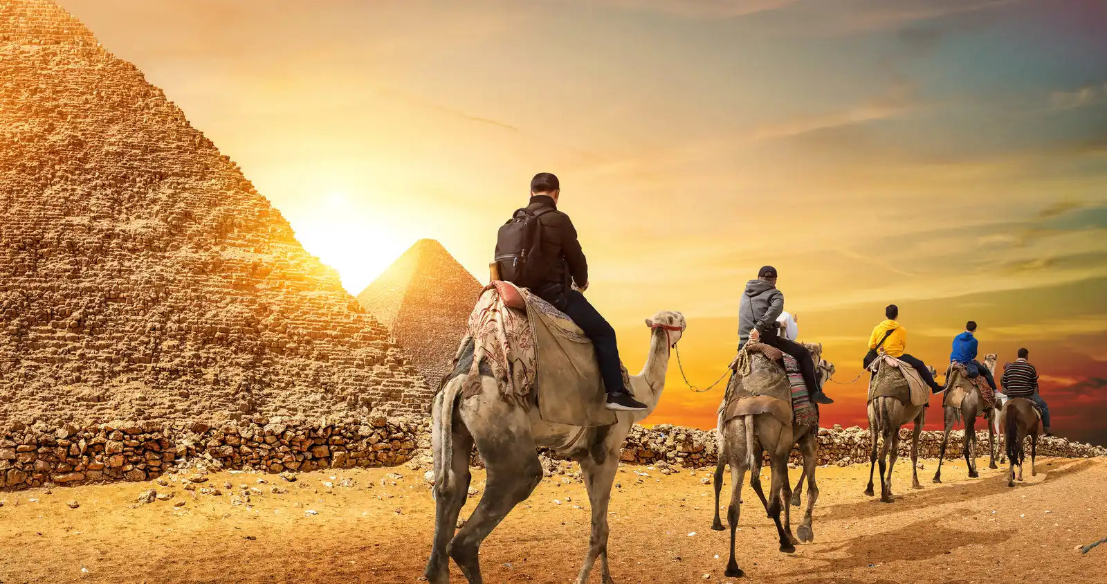 Camel caravan traveling past the pyramids at sunset.
